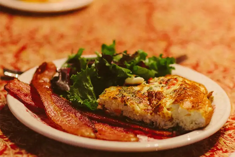 A gourmet breakfast plate featuring a fresh vegetable frittata, crispy bacon, and a side salad at The Buckingham Inn in Madison, WI.